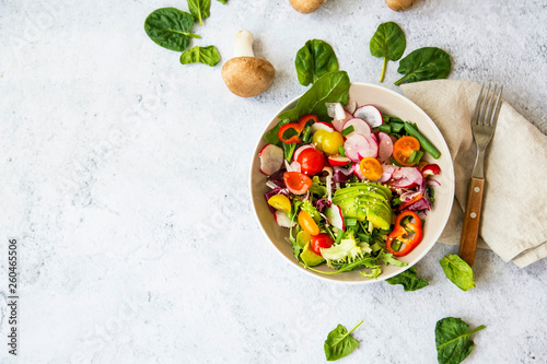 Healthy salad with bio organic vegetables, green vegan meal with avocado, pepper, radish, tomatoes, lettuce, cabbage, spring colorful salad closeup, clean eating concept top view