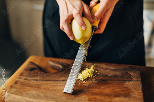 Female chef grating lemon zest on a wooden board