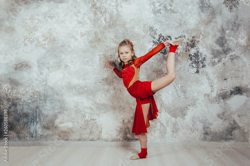 Girl gymnast in a red gymnastic swimsuit posing on studio background