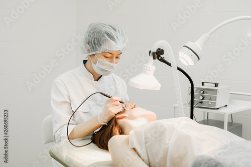 Medical treatment removal of birthmark from female patient's face. Female dermatologist surgeon using a professional electrocautery for removing mole. Radio wave electrocoagulation remove method