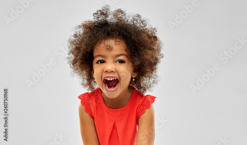 emotion, childhood and expression concept - happy laughing little african american girl over grey background