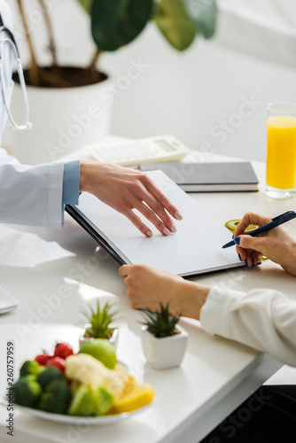 cropped view of nutritionist holding clipboard near patient with pen