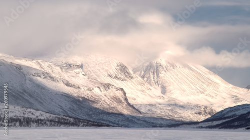 Swedish Lapland mountain landscape in winter with snow and cloud covered peak Kuoperatjakka in Sjaunja Naturreservat during sunset with frozen lake in foreground