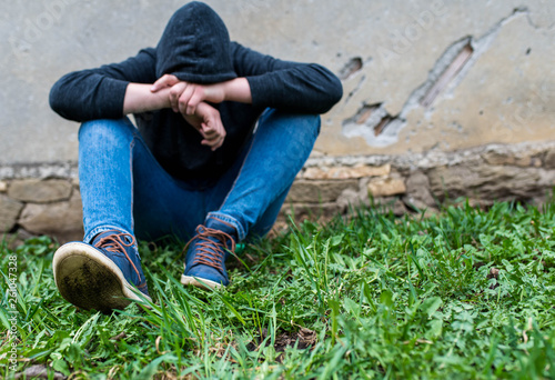 Frustrated teenage boy sitting near a crumbling wall at the correctional institute, focus on the boys shoe.