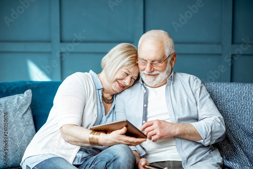 Lovely senior couple dressed casually using digital tablet while sitting together on the comfortable couch at home