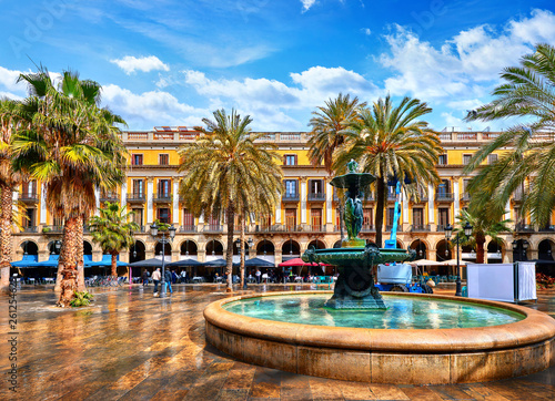 Royal area in Barcelona, Spain. Fountain with statues and high palm trees among traditional Spanish architecture at main central square of old town. Summer landscape with blue sky and clouds.