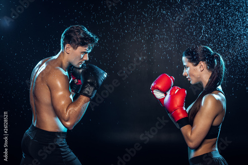 Side view of two boxers in boxing gloves training together under water drops on black