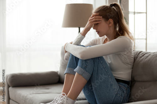 Upset woman frustrated by problem sitting on couch, embracing knees,