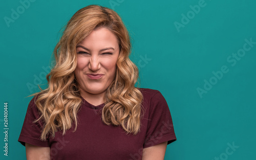 A young woman is squinting a sour grimace while standing against blue background.