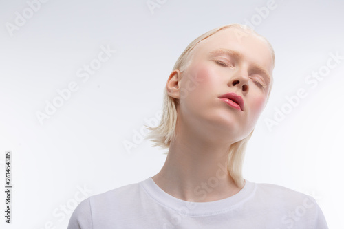 Skinny young model with rosy cheeks closing eyes while posing