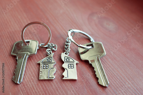 Two keys with splitted or broken key rings with pendant in shape of house divided in two parts on wooden background with copy space. Dividing house when divorce, division of property, real estate heri