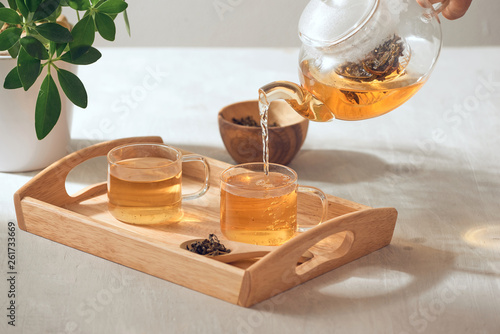 A hand pouring tea from glass teapot on wooden serving tray