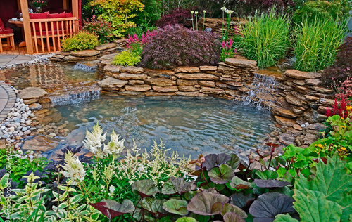The pond area in an aquatic garden with planted rockery and waterfalls and summer house