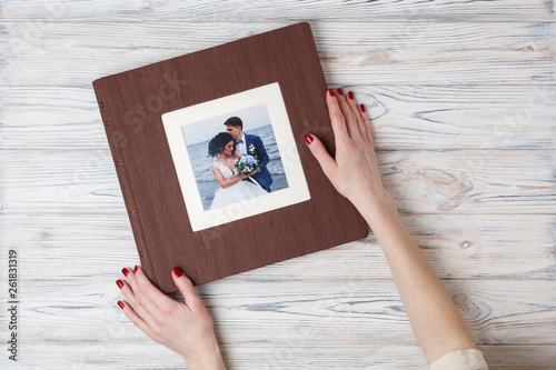 brown photo book with leather cover. stylish wedding photo album. a person opens a photobook. Family photoalbum on the table. the womans hand holding a family photo album