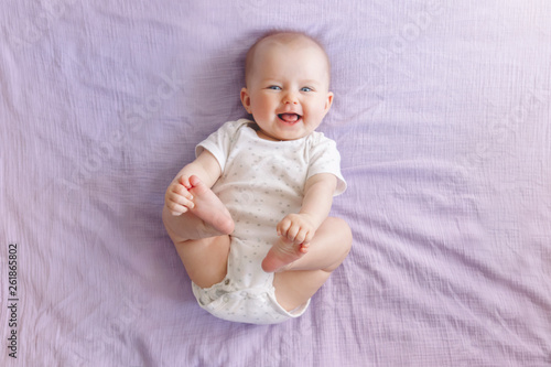 Portrait of cute adorable smiling laughing white Caucasian baby girl boy with blue eyes four months old lying on bed looking at camera. View from top above. Happy childhood lifestyle.