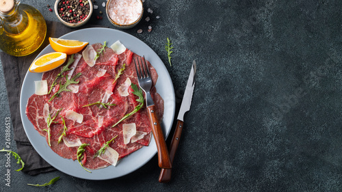 Marbled beef carpaccio with arugula, lemon and parmesan cheese on dark concrete table. Top view, flat lay with copy space