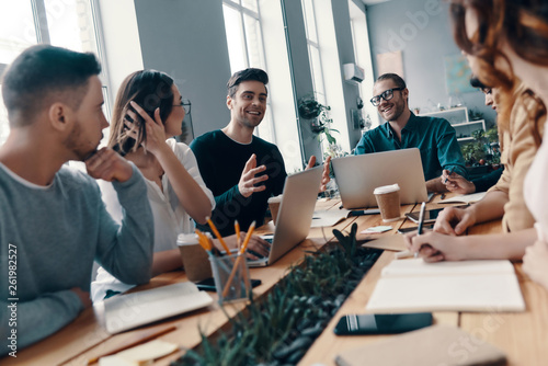 Achieving success together. Group of young modern people in smart casual wear discussing something and smiling while working in the creative office