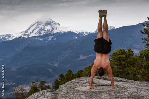 Fit and Muscular Young Man is doing exercises on top of the Mountain during a cloudy day. Taken on Chief Mountain in Squamish, North of Vancouver, BC, Canada.