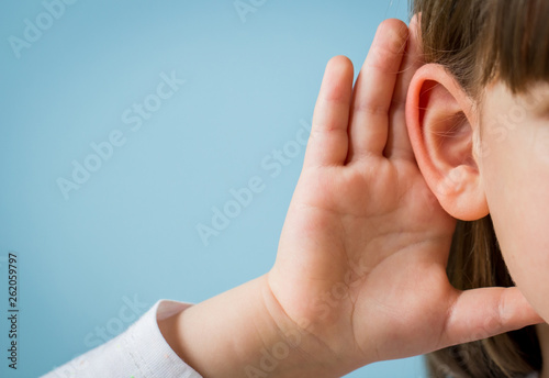 Little girl with hearing problem on light blue background. Close up, copy space.