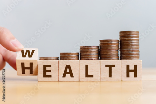 Hand flip wooden cube with word wealth to health with coins stack step up growing growth value. Investment in life insurance and healthcare concept