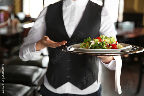 Young female waiter with salad in restaurant, closeup