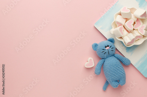 A small knitted baby toy-cat, nitebook and sweetness marshmallow on pink pastel background, flat lay, top view, copy space