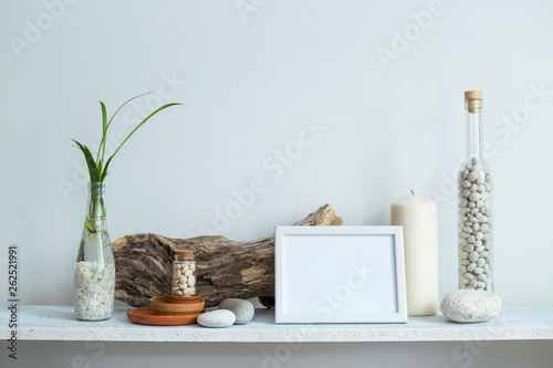 Shelf against white wall with decorative candle, glass, wood and rocks. Home plant in pot.