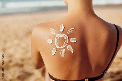 Skin care. Sun protection. Woman apply sun cream. Woman With Suntan Lotion On Beach In Form Of The Sun. Portrait Of Female With Drawn Sun On A Shoulder. Suncream. Girl Holding Moisturizing Sunblock.