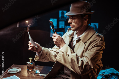 Detective in trench coat looking at photo through magnifier