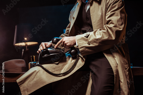 Partial view of man in trench coat holding telephone in office