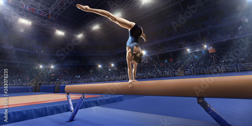 Female athlete doing a complicated exciting trick on gymnastics balance beam in a professional gym. Girl perform stunt in bright sports clothes