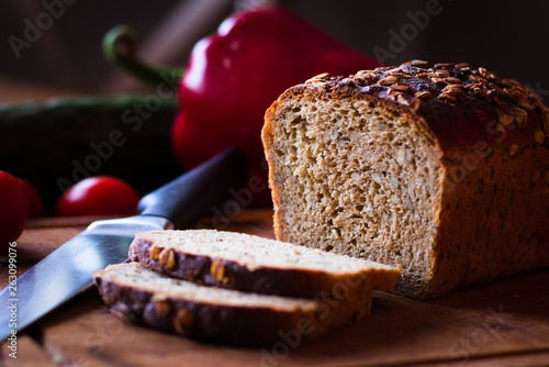 bochenek chleba, dwie kromki na desce na tle noża i warzyw