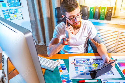 graphic designer testing the application on the tablet. Design for mobile devices. Portrait of young designer sitting at graphic studio in front of laptop and tablet while working online.