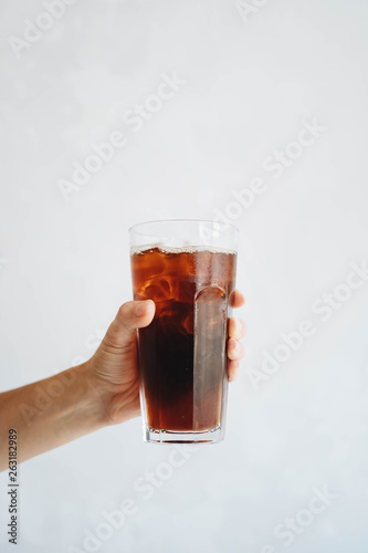 Hand holding a glass of homemade cold brew coffee on white table