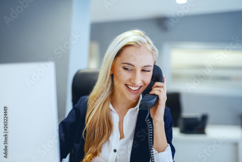 Smiling beautiful Caucasian businesswoman having phone call while sitting in office. Great minds think independently, not alike.