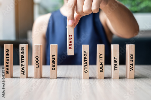 Businesswoman hand placing or pulling wooden Dominoes with BRAND text. and Marketing, Advertising, Logo, Design, Strategy, Identity, Trust and Values. Product development concept