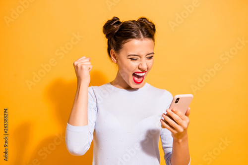 Portrait of delighted thrilled excited screaming lady impressed by news feed in her social network account raising fists isolated on vibrant background in white clothing