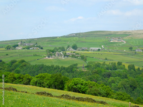 west yorkshire dales scenery with farmhouses perched on high hills with typical walled fields and midgley moor in the distance with blue sunlit summer sky with farmhouses in the pecket well area