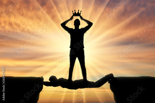 Selfish man puts a crown on his head, he stands on a man in the form of a bridge over a precipice