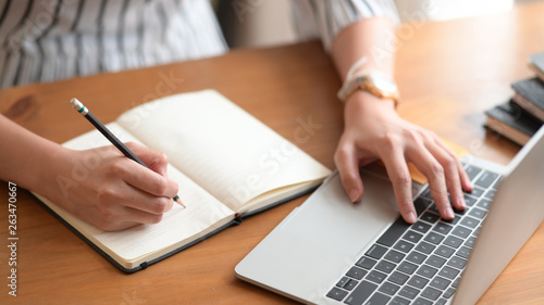 Businesswoman writing note while using laptop at table in office