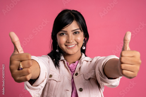 portrait of beautiful asian woman showing two thumbs up over pink background