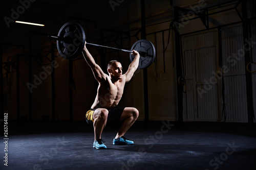 Athletic man training squats with barbells over head