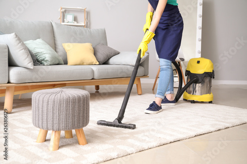 Female janitor with vacuum cleaner in room