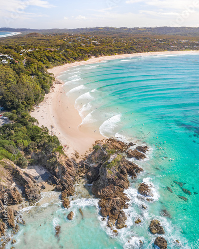 Aerial shot at sunrise over the ocean and white sand beach with swimmers and surfers enjoying summer