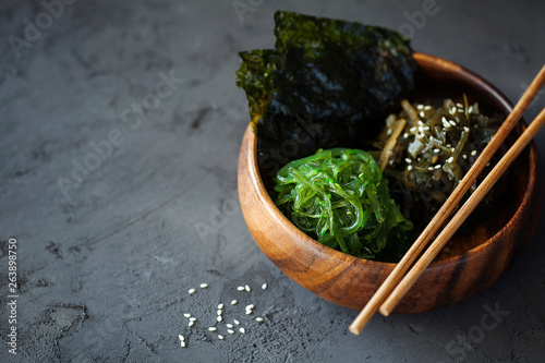 Traditional Japanese Snack - Chuka Wakame seaweed salad and crispy roasted nori sheets in wooden bowl on dark background top view with copy space for text.Healthy seafood high in vitamins