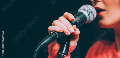 Singer at microphone. Woman singing and holding mic. Female vocal talent. Music show recital.