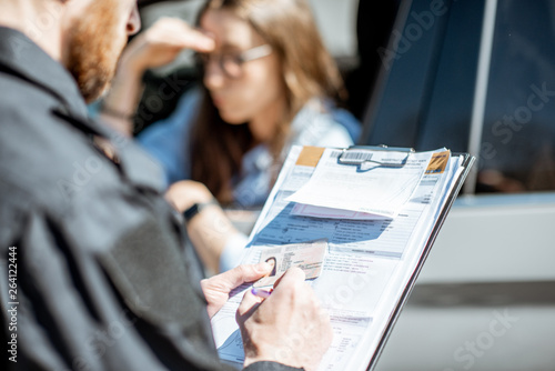 Policeman issuing a fine for violating the traffic rules to a young woman driver, close-up view focused on the folder