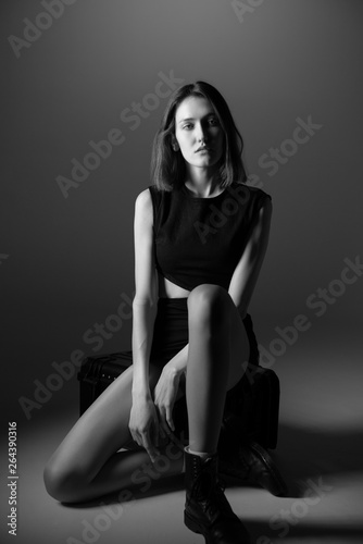 Fashion model. Young woman posing in studio wearing black drees and boots. Beautiful caucasian girl over gray background