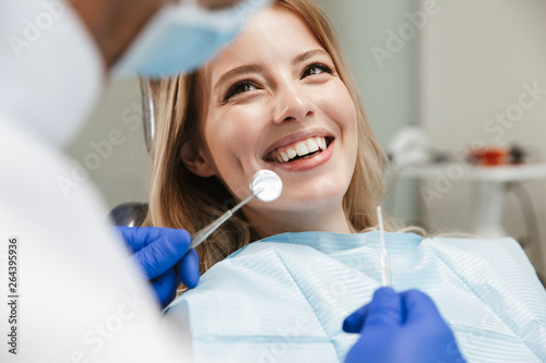 Image of pretty woman sitting in dental chair while professional doctor fixing her teeth