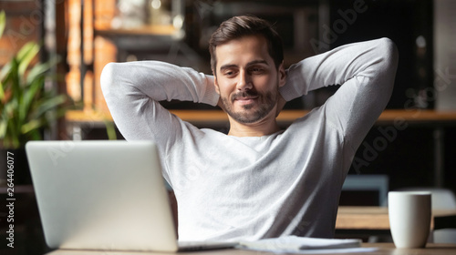 Serene businessman sitting at table feels satisfied accomplishing work